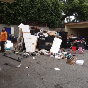 A man next to a large pile of household junk and an overflowing dumpster for Vic's Haul Away & Junk Removal Service in Garden Grove, CA.