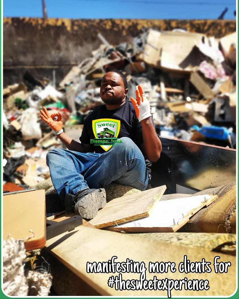 A Sweet Dumps Junk team member sits in a truck filled with removed junk, with a large pile of debris in Los Angeles, CA.