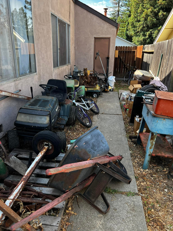 A cluttered backyard filled with old lawnmowers, a bicycle, and various rusty items, awaiting junk removal by We Haul It All in Lakeland, FL