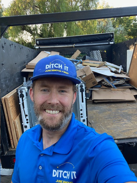 A Ditch it employee smiling in front of a truck loaded with various junk items in Martinez, CA.