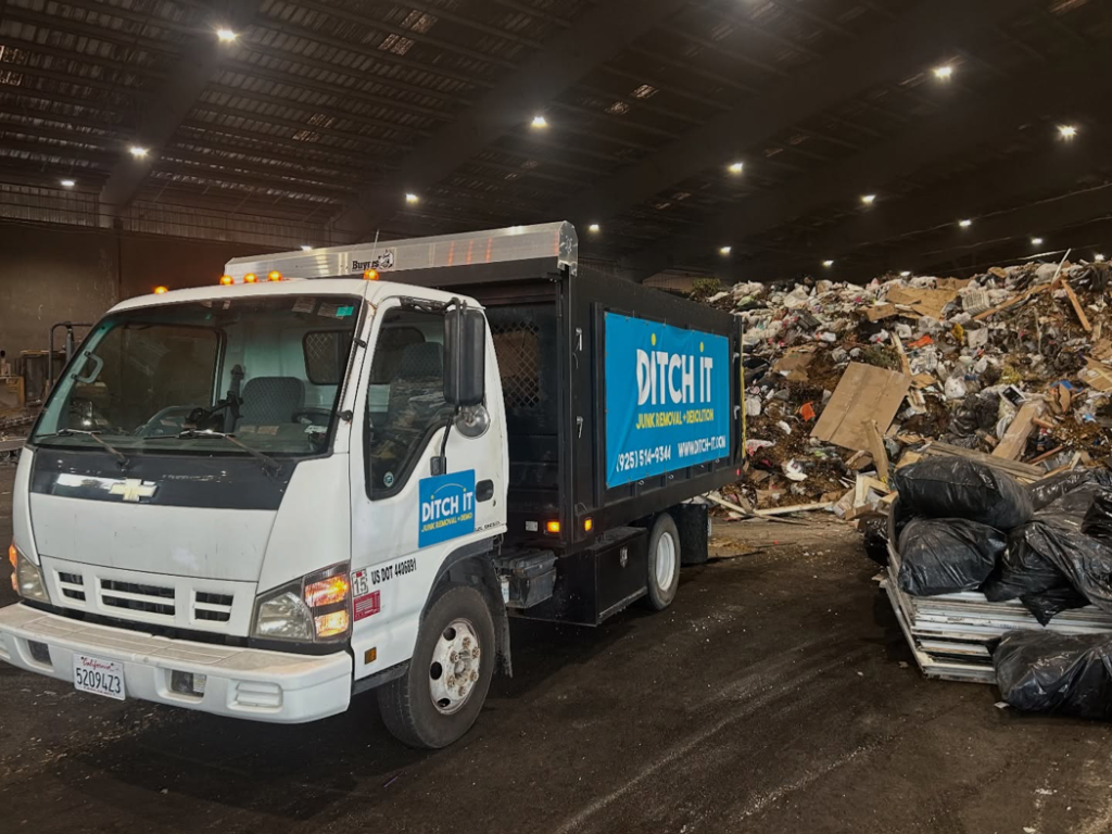 A Ditch it junk removal truck at a waste transfer station with large piles of debris in Martinez, CA.