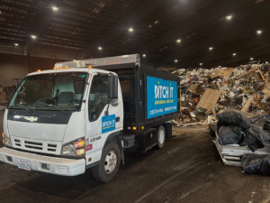 A Ditch it junk removal truck at a waste transfer station with large piles of debris in Martinez, CA.