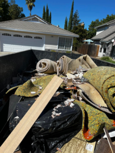 A large dumpster filled with construction debris and old carpet rolls from a junk removal job by We Haul It All in Lakeland, FL