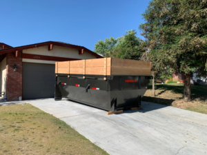 An empty junk removal dumpster with wooden extensions ready for use in a residential driveway from Kern County Clean Up in Bakersfield, CA.
