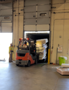 A forklift operator loading a large stack of mattresses into a shipping container for The Mattress Guy in Oakland, CA.