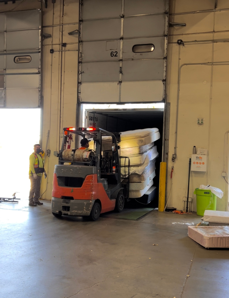 A forklift operator loading a large stack of mattresses into a shipping container for The Mattress Guy in Oakland, CA.