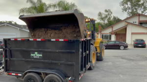A front-end loader dumping dirt into a trailer for SD Junk Takers Hauling and Junk Removal in San Diego, CA.