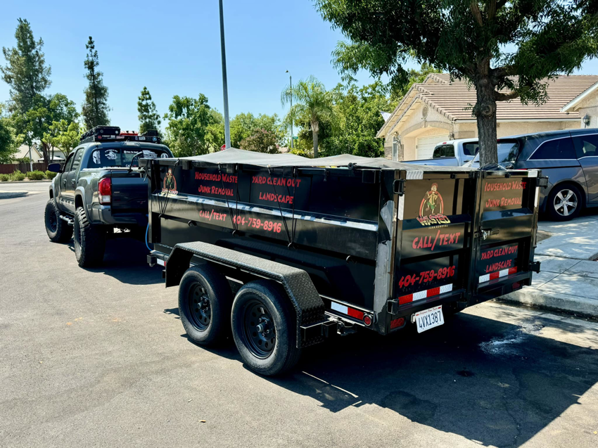 A Wasted Junk Removal truck with a loaded trailer covered by a tarp, ready for transport in Fresno, CA.