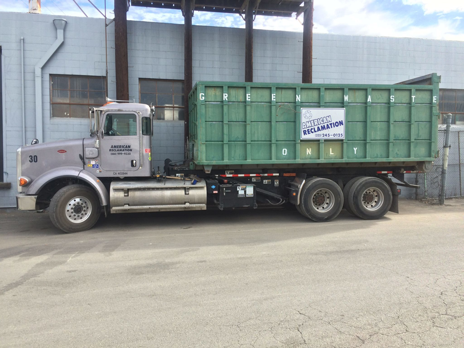 A junk removal truck with a green roll-off dumpster for American Reclamation in Los Angeles, CA