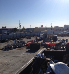 An outdoor yard filled with various junk and scrap piles, including a large container, at MEC Recycling LLC in Bakersfield, CA.