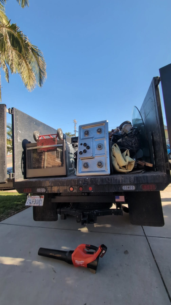 A Junk Rush truck loaded with an oven, black trash bags, and various debris after a general junk removal job in San Diego, CA.