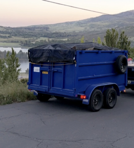 A close-up of a loaded blue dump trailer with a tarp, used for general junk removal by Posche Hauling Services in San Diego, CA.