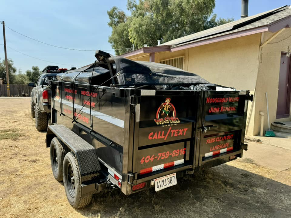 A Wasted Junk Removal truck and trailer loaded with items, ready for disposal in Fresno, CA.