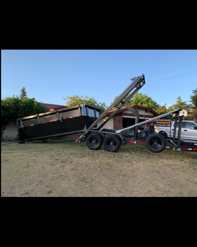 A truck efficiently lowering a black junk removal dumpster onto a residential lawn by Kern County Clean Up in Bakersfield, CA.