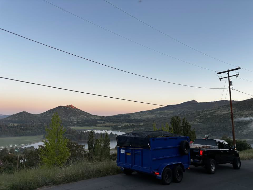 A truck towing a loaded blue dump trailer with a tarp, ready for junk removal by Posche Hauling Services in San Diego, CA.