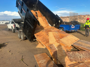 A dump trailer from Bakersfield Roll-Off Service unloading construction debris with a worker present in Bakersfield, CA.