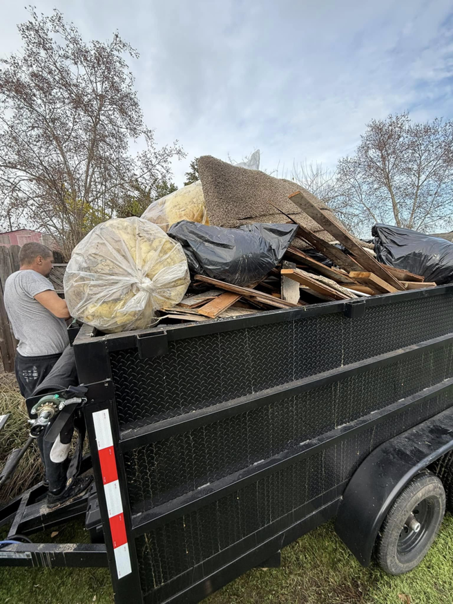 A worker loading construction debris and insulation into a dump trailer for Junk Away & Cleaning in Sacramento, CA.