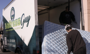 Two workers loading old mattresses into a branded truck for The Mattress Guy's removal service in Oakland, CA.